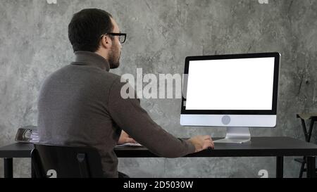 Bearded young businessman woking on computer. White Display. Stock Photo