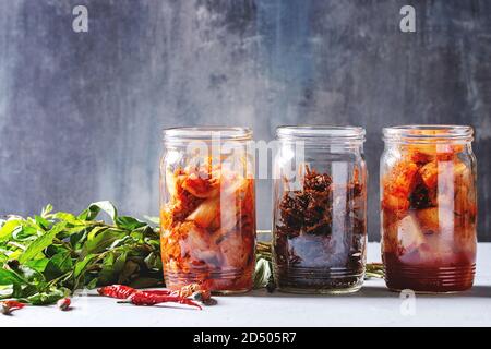 Korean traditional fermented appetizer kimchi cabbage and radish salad, hot spicy anchovies fish snack served in glass jars with Vietnamese oregano gr Stock Photo