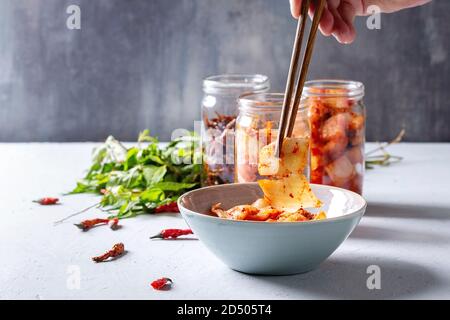 Korean traditional fermented appetizer kimchi cabbage and radish salad, fish snack served in glass jars with Vietnamese oregano and chili peppers over Stock Photo