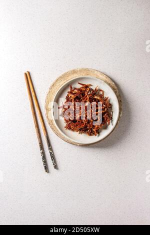 Vietnamese traditional hot spicy anchovies fish snack in ceramic plates with chopsticks over grey spotted background. Flat lay, space. Stock Photo