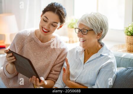 Young and senior women are using tablet pc. Daughter is helping mother having fun staying at home. Stock Photo