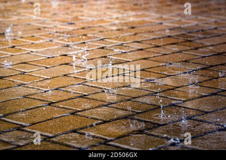 Raindrops on street tile wet floor in city during rain. City sidewalk in rainy day. Stock Photo