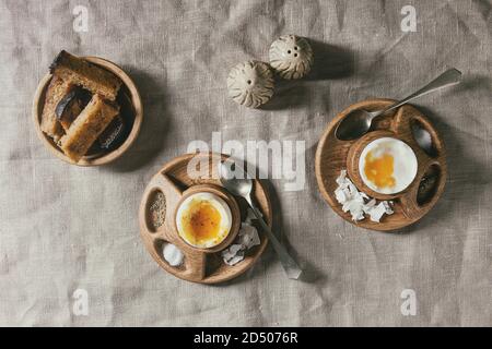 Breakfast with soft boiled eggs, served in wooden egg cup with salt, pepper and toasted bread over linen tablecloth. Flat lay, space Stock Photo