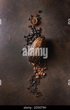 Variety of fresh and dry cocoa beans and cocoa pod with chopped dark chocolate and cocoa powder over brown texture background. Flat lay, space Stock Photo