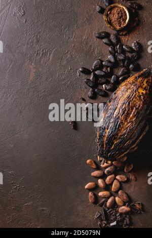 Variety of fresh and dry cocoa beans and cocoa pod with chopped dark chocolate and cocoa powder over brown texture background. Flat lay, space Stock Photo