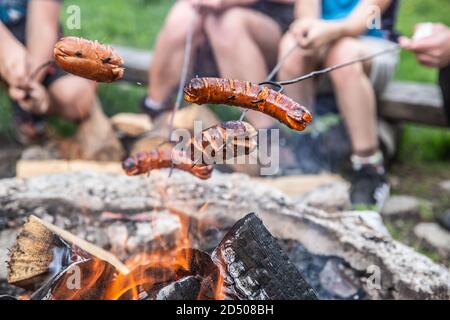 Friends roast sausages over an open fire outdoors Stock Photo