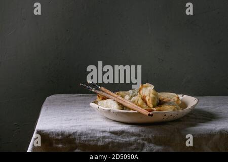 Fried asian dumplings Gyozas potstickers in white ceramic plate served with chopsticks over linen table cloth. Asian dinner Stock Photo