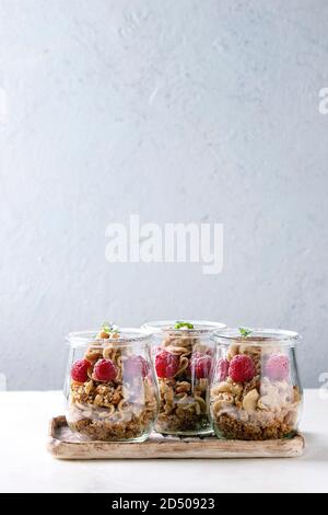 Layered dessert in jars. Biscuit, coffee cream, nuts, raspberries, fresh mint. Served on ceramic tray over white marble table. Stock Photo