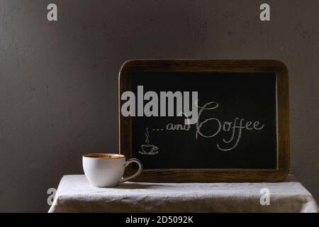 Cup of espresso coffee standing on linen table cloth. Vintage chalkboard with lettering behind Stock Photo