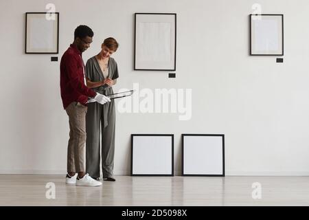 Full length portrait of two art gallery workers looking at painting frames while planning exhibition in museum, copy space Stock Photo