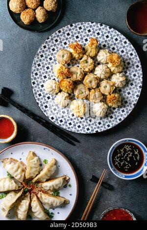 Dim sum Gyozas asian fried dumplings party set with variety of sauces served in ceramic plates and bowls with chopsticks, tea cups over dark blue text Stock Photo