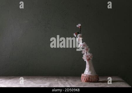 Spring blossom cherry branch flowers in craft ceramic vase standing on grey linen table cloth. Spring interior. Copy space. Stock Photo