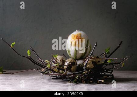Quail Easter eggs in birds nest with standing on grey linen table cloth with concrete wall at background. Easter holidays interior decorations. Stock Photo