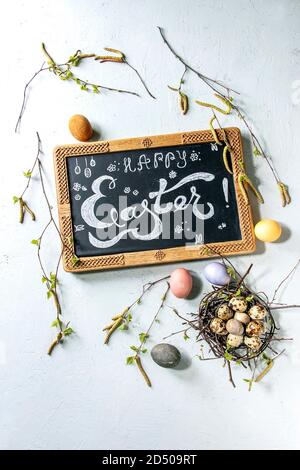 Chalkboard with Easter hand lettering, colored chicken and quail eggs in birds nest, handmade craft wool felted and ceramic eggs, birch branches over Stock Photo