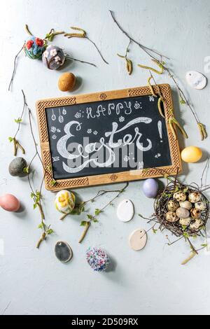 Chalkboard with Easter hand lettering, colored chicken and quail eggs in birds nest, handmade craft wool felted and ceramic eggs, birch branches over Stock Photo