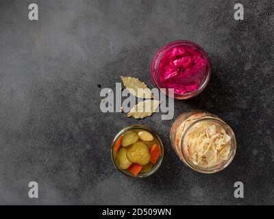 assortment of fermented vegetables: cabbage, cucumbers, carrots, in glass jars. dark concrete background, top view, copy space Stock Photo