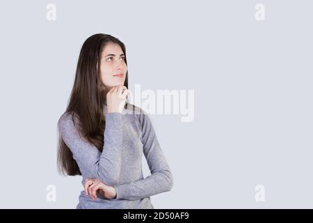 Portrait of thoughtful  student girl  looking up and  holding hand under chin isolated on white background. Positive student girl thinking of a soluti Stock Photo