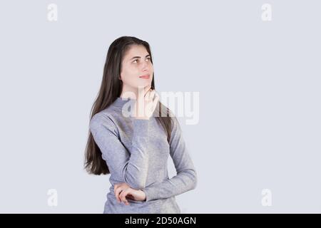 Portrait of thoughtful  student girl smiling  looking up and  holding hand under chin isolated on white background. Positive student girl thinking of Stock Photo