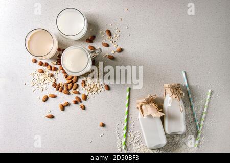 Variety of non-dairy vegan lactose free nuts and grain milk almond, hazelnut, coconut, rice, oat in glass bottles with straws and ingredients above ov Stock Photo