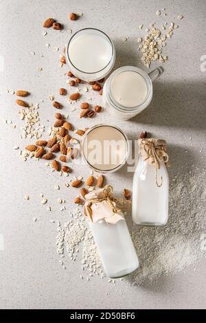 Variety of non-dairy vegan lactose free nuts and grain milk almond, hazelnut, coconut, rice, oat in glass bottles with ingredients above over white sp Stock Photo