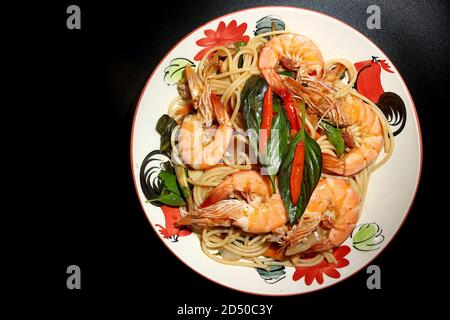 Stir fried spaghetti with chili paste, shrimp, basil, fresh chili, Young green peppercorns, onion, carrot, kaffir lime leaves. Put in a plate on a bla Stock Photo