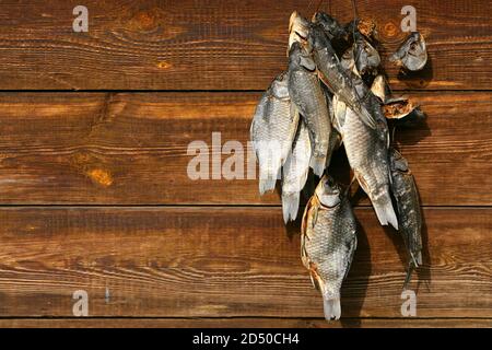 A bunch of dried salted fish hangs on a background of wooden planks Stock Photo