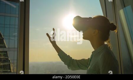 VR, sightseeing, discover, technology concept. Woman using virtual reality headset and moving hand against view on cityscape from panoramic skyscraper Stock Photo