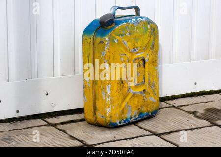 An old yellow metal canister stands against a white wall. Container with flammable liquid in an open space Stock Photo