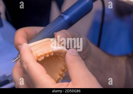 Professional dental technician or dentist holding motor handpiece tool and working with dental prosthesis, tooth dentures - close up view. Stomatology Stock Photo