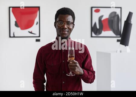 Waist up portrait of smiling African-American man holding champagne glass and looking at camera at art gallery opening, copy space Stock Photo
