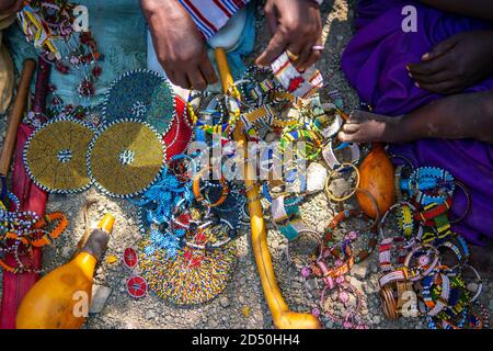 Masai Tribal Female Makes a Colorful Souvenir Bijou for sale for tourist. Bracelets, Nacklaces and Rings Made of Beads by African Women Stock Photo