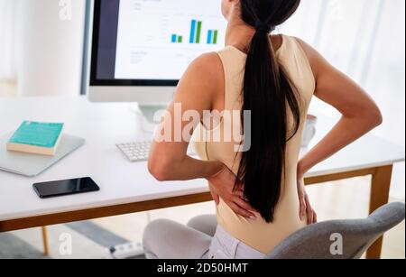 Overworked woman with back pain in office with bad posture Stock Photo