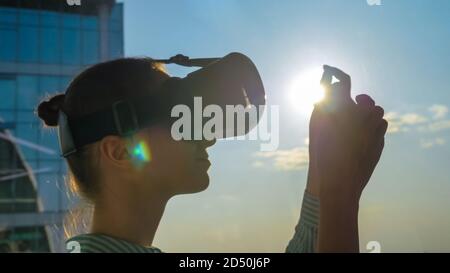 VR, sightseeing, discover, technology concept. Woman using virtual reality headset and moving hand against view on cityscape from panoramic skyscraper Stock Photo