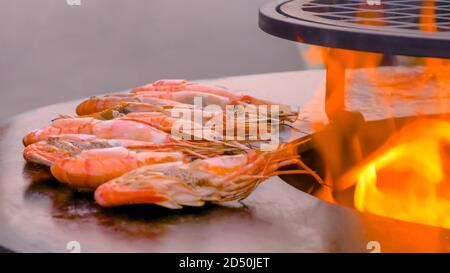 Process of grilling fresh red king prawns on round black brazier at summer local food market - close up view. Outdoor cooking, barbecue, gastronomy Stock Photo