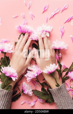 Delicate young hands on a pink pastel background in a sweater with chrysanthemum flowers in the sleeves. Winter body care concept, moisturizing and wrinkle prevention. Stock Photo