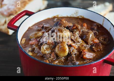 Beef Bourguignon cooked in an enameled cast iron Dutch oven and served with homemade artisan bread over a rustic wood background. Stock Photo