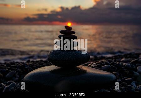 Stacked pebble stones on the background of a bright cloudy sky at sunset and the sea. Zen pebble pyramid, background, harmony and balance concept