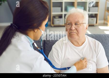 Female doctor listening to white-haired male patient's heart through stethoscope Stock Photo