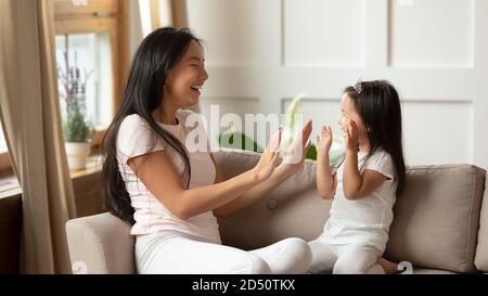 Smiling young mother and little daughter clapping hands on couch Stock Photo