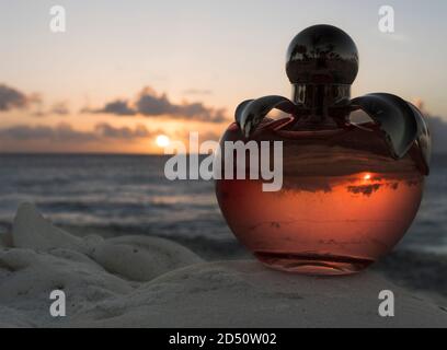A glass bottle of perfume where the sunset can be seen on the beach of Bonaire Stock Photo