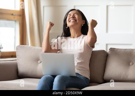 Overjoyed young Asian woman celebrating success, using laptop Stock Photo