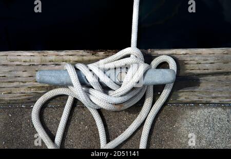 Mooring rope tied off around metal bitt, attached to aged wood. Stock Photo