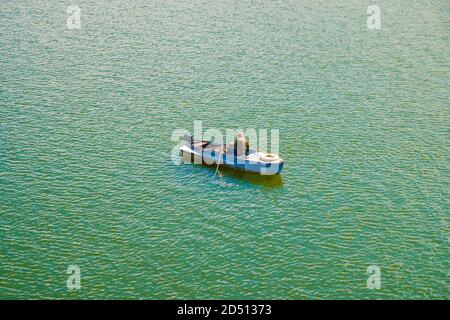 A lone fisherman in military uniform on a boat among the green water. View from above Stock Photo