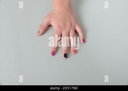 close up of young woman's fingernails painted different pretty colors, one hand on grey background Stock Photo