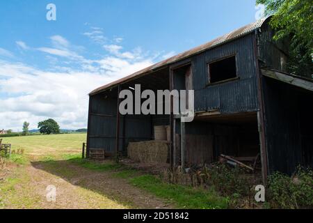 Rusty old farm barn made of corrugated metal storing hay bales, inside in field with deep blue sky and sweeping clouds in late summer sunshine Stock Photo