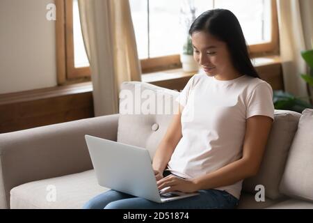 Smiling Asian young woman using laptop at home Stock Photo