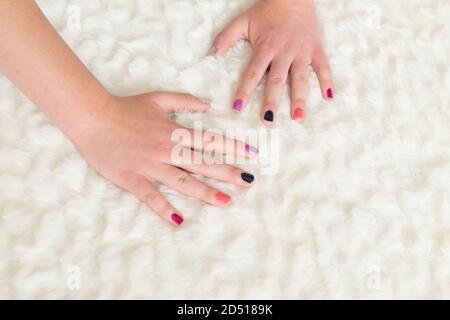 close up of young woman's fingernails painted different pretty colors. two hands on winter white fluffy  background Stock Photo