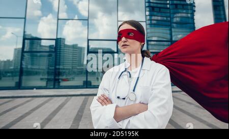 female paramedic in a superhero raincoat standing on a city street. Stock Photo