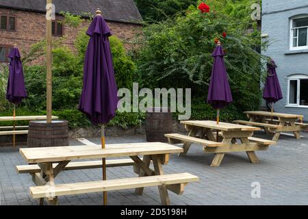close up of empty wooden tables and chairs with closed purple umbrellas outside restaurant with social distancing measures in autumn Stock Photo
