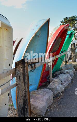close up of pretty blue, green and red upside down small boats leaning against a wooden fence in summer sunshine with blue sky and white clouds Stock Photo